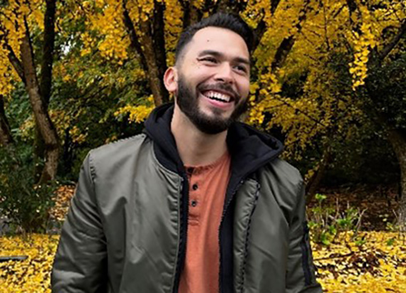 A headshot of Jessi Hinestrosa smiling.against an autum background.